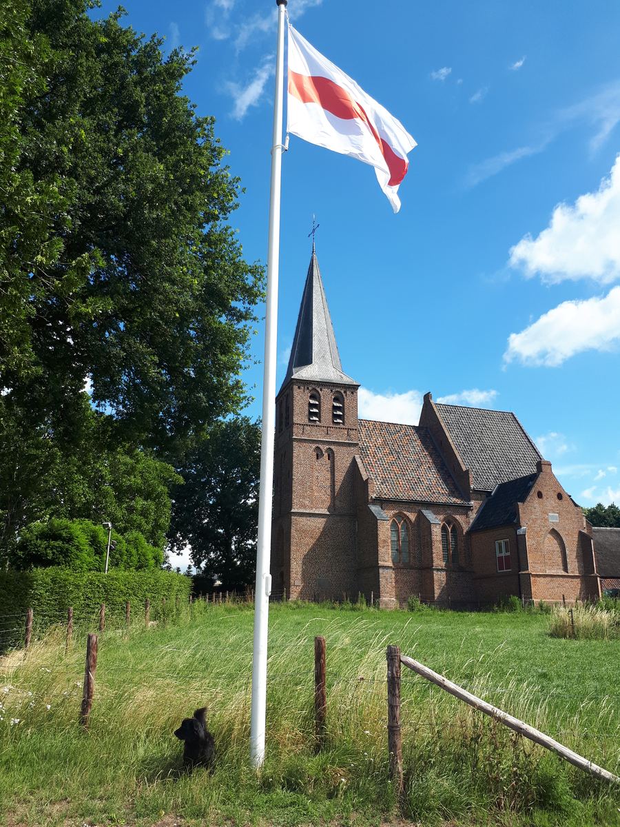 Het kerkje van Persingen met de vlag in top, gezien vanaf de polder
